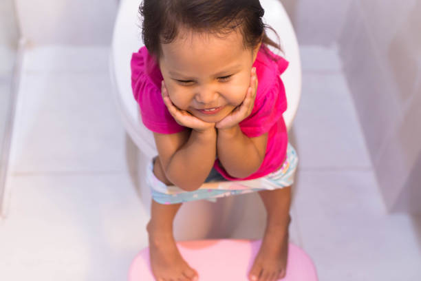 Toddler happy sitting on the toilet. Potty training. A little female child sitting on the big toilet in a white bathroom, smiling and trying to go pee. constipation child stock pictures, royalty-free photos & images